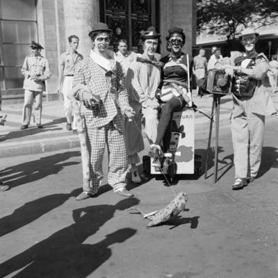 Carnaval de rua, homens fantasiados de mulher e de fotógrafo lambe-lambe