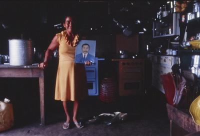 Mulher em cozinha posa com retrato de homem