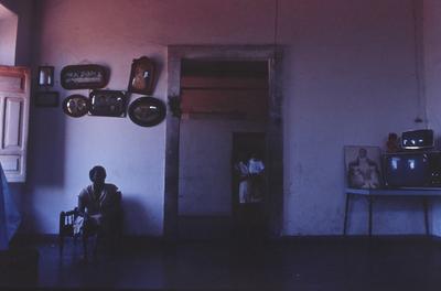 Mulher não identificada em sala, ao fundo reproduções de daguerreótipos