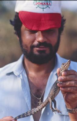 Homem não identificado com filhote de jacaré nas mãos