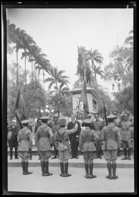 Washington Luís, ao centro, entre civis e militares; ao fundo, a estátua equestre de Duque de Caxias
