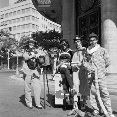 Carnaval de rua, homens fantasiados de mulher e de fotógrafo lambe-lambe